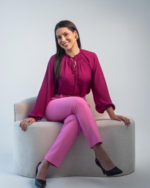 Luana Amaral de blusa vinho, sentada e sorrindo